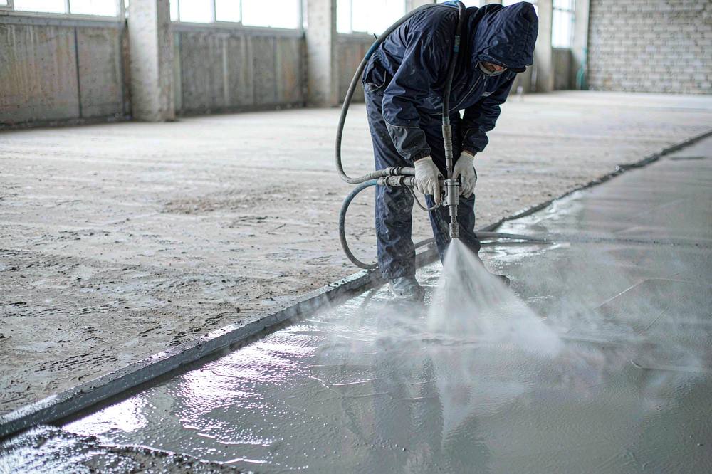 worker spraying grey polyurea floor coating onto a concrete slab in a warehouse