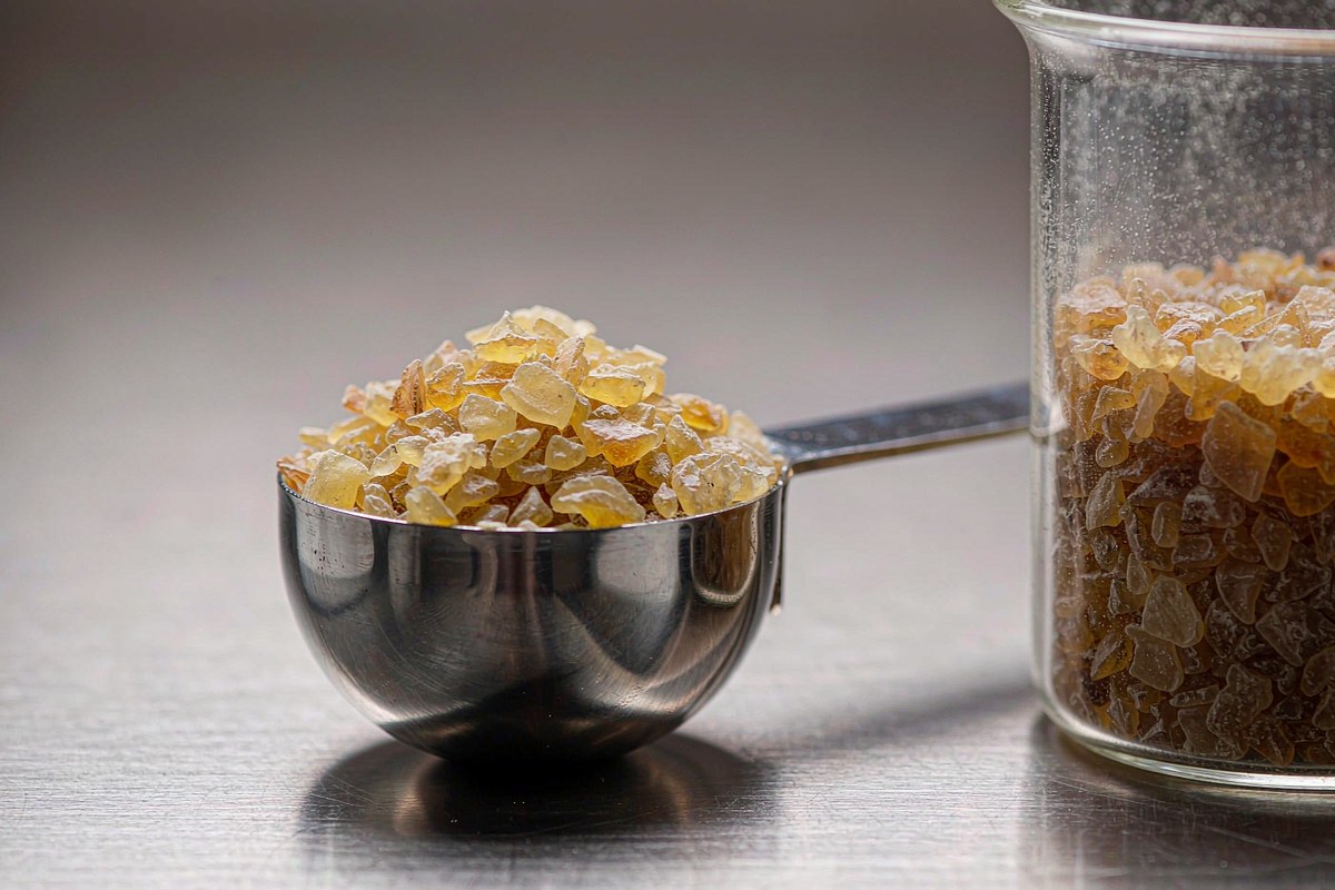 pale amber solid epoxy resin flakes in a stainless steel scoop beside a glass beaker on a laboratory bench