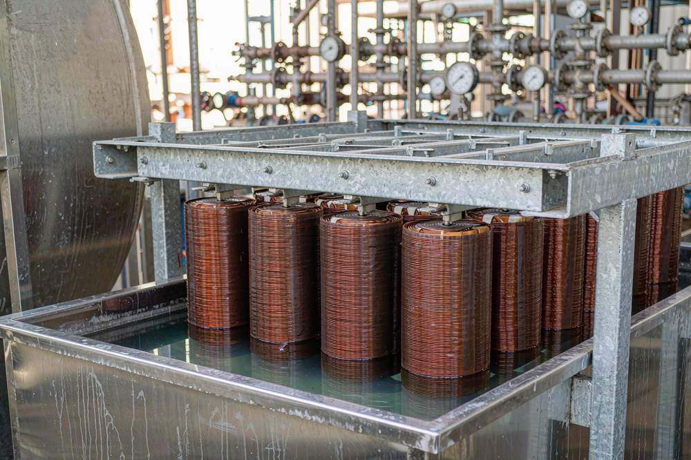 copper wound transformer coils on a rack lowered into a stainless steel vacuum impregnation tank of clear resin